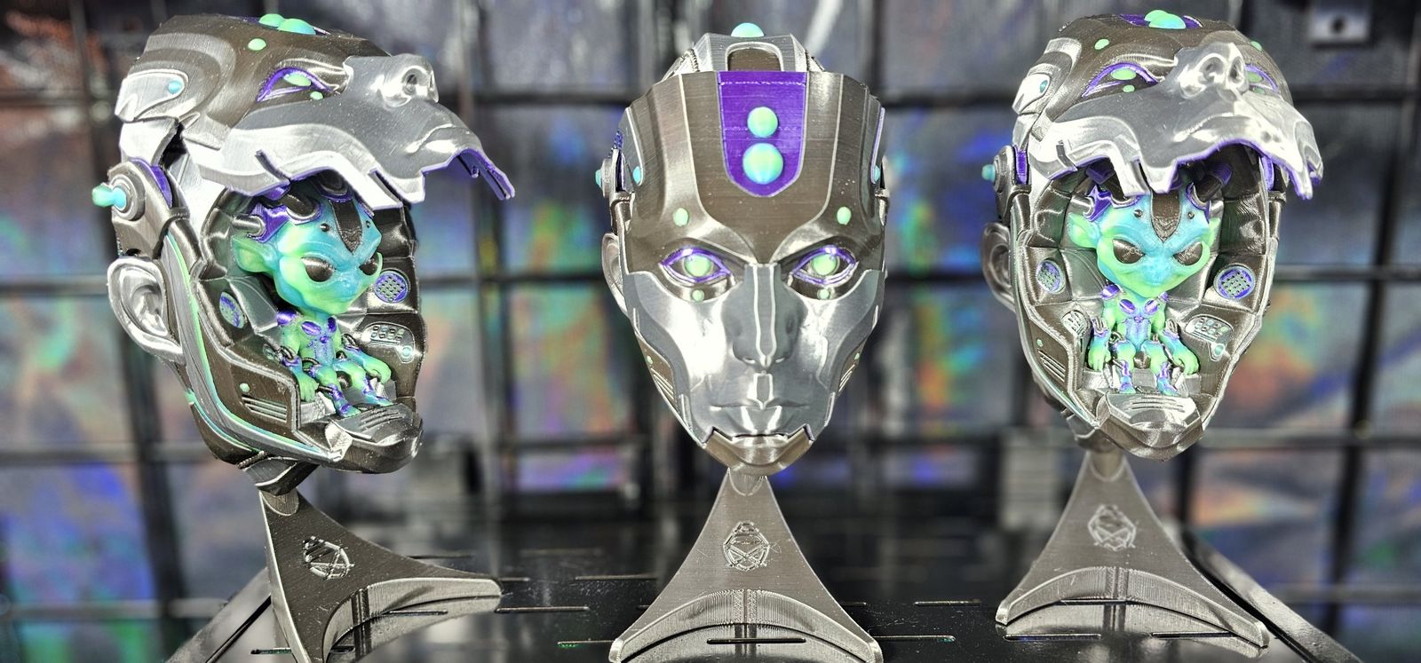Three silver cyborg heads on stands, two opened to show small green alien pilots inside