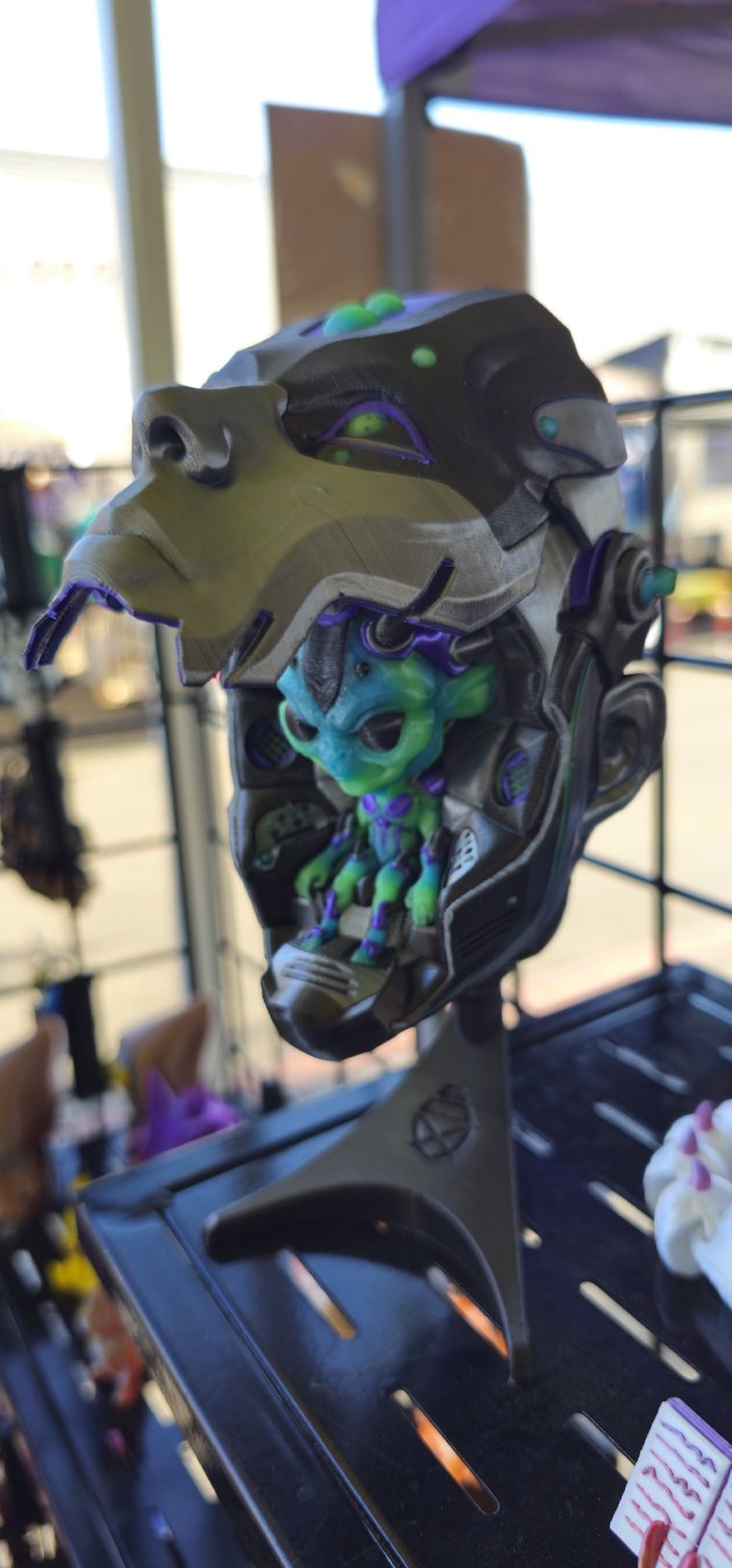 Open cyborg head on a stand with a green alien pilot seated inside