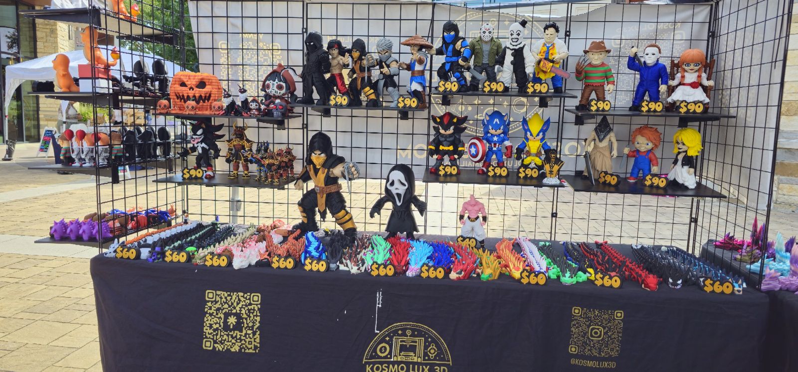 Outdoor Kosmo Lux 3D booth with two shelves of figures and a long row of articulated dragons