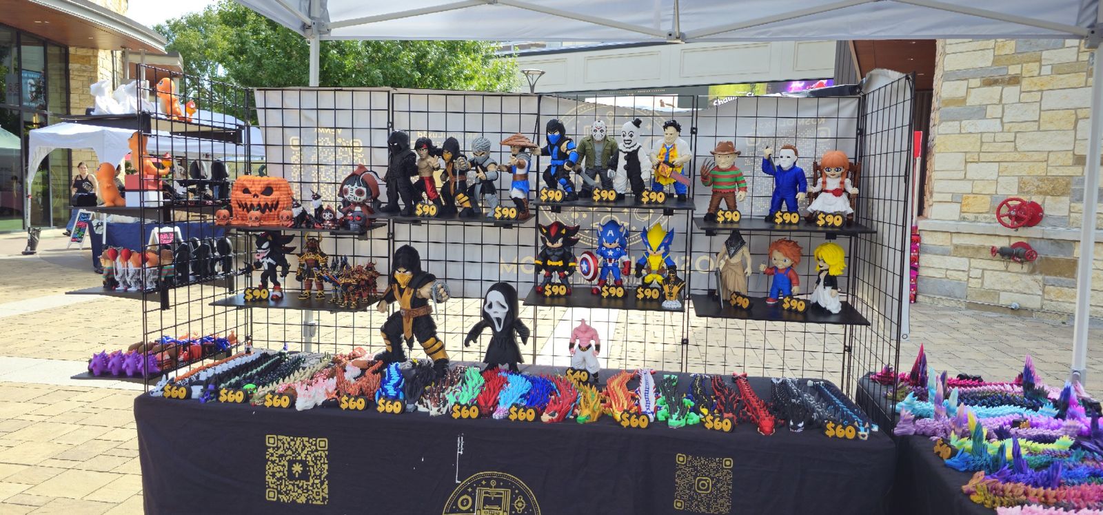 Kosmo Lux 3D outdoor market booth with shelves of printed figures and a table full of articulated dragons